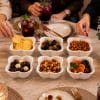 A set of 6 white flower-shaped ceramic bowls filled with various snacks, arranged on a dining table during a gathering.