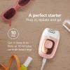 A flat-lay image featuring a glossy pink and rose gold VGR-brand epilator, plugged into a white cord, with a digital display reading 100%. Next to it are pink sunglasses, a bottle of yellow nail polish, an orange strap, and a cleaning brush. Overlaid text says 