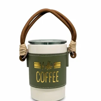 A portable white ceramic coffee mug with a green leather sleeve, gold "Hello Coffee" lettering, and a brown rope carry strap, displayed