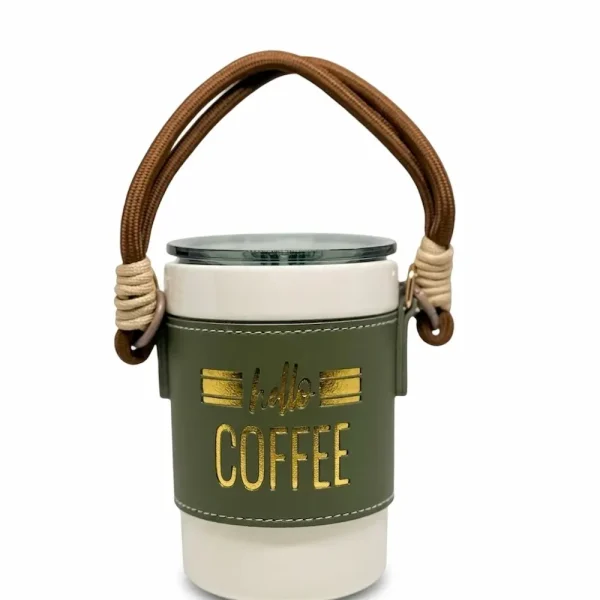 A portable white ceramic coffee mug with a green leather sleeve, gold "Hello Coffee" lettering, and a brown rope carry strap, displayed
