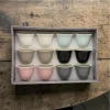A 12-piece set of multicolored ceramic Arabic coffee cups in a gift box placed on a kitchen table.