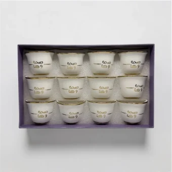 A 12-piece set of white ceramic Arabic coffee cups with gold "صحة وهنا" calligraphy in a gift box,