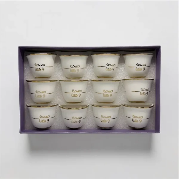 A 12-piece set of white ceramic Arabic coffee cups with gold "صحة وهنا" calligraphy in a gift box,