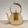 A beautiful honey-toned glass teapot with a gold metal infuser and a wooden handle