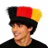 A young man wearing a vibrant black, red, and gold faux fur hat representing Germany's national football team colors, isolated on a white background.