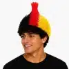A young man wearing a vibrant black, red, and yellow spiked mohawk hair wig representing Germany's football team colors, isolated on a white background.