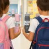 Two kids holding pink and gray insulated travel mugs with school backpacks